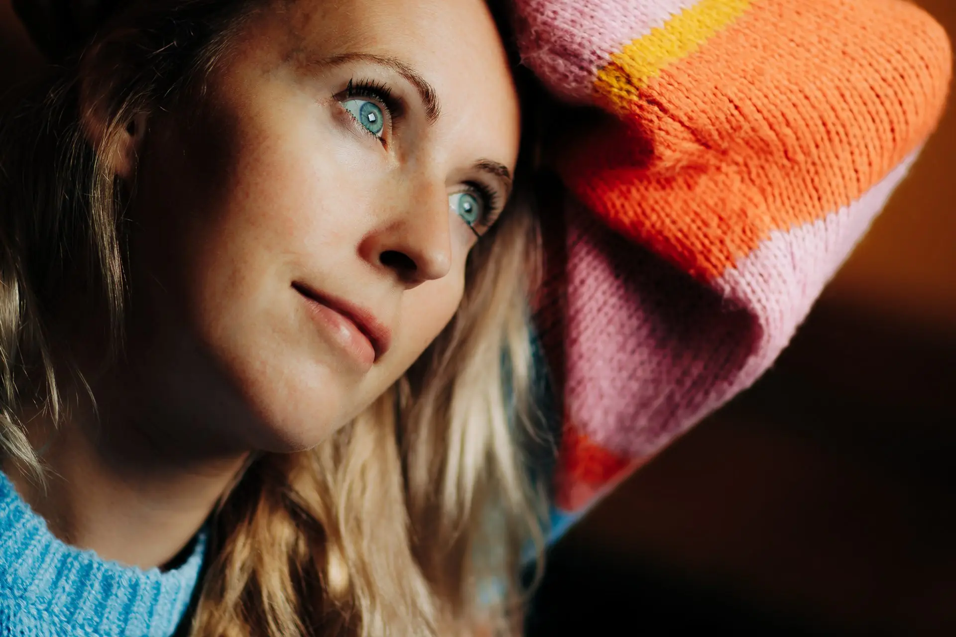 Petra Harrington looks up and away, a pink and orange striped knitted sleeve at her shoulder.