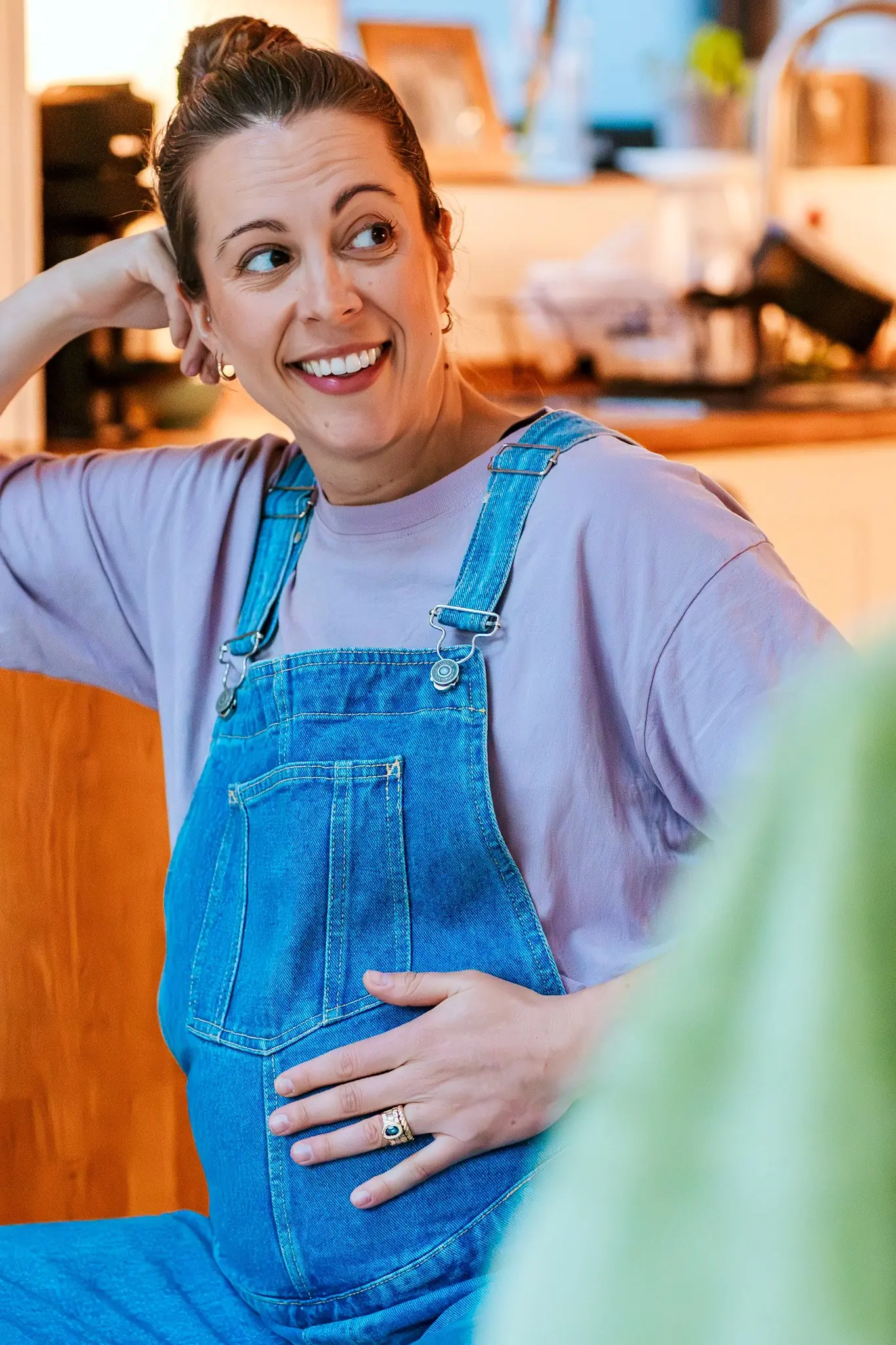 A woman in denim dungarees laughs, one hand resting on her bump.
